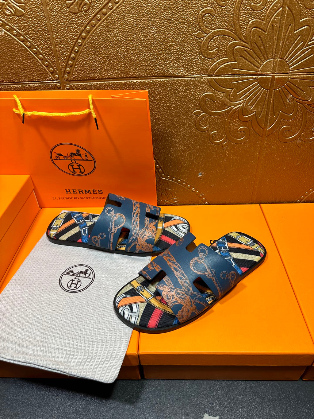 Blue Hermes logo slide sandals with patterned straps and open toe, pair resting.