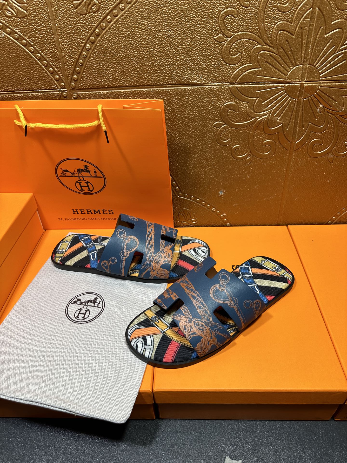 Blue Hermes logo slide sandals with patterned straps and open toe, pair resting.