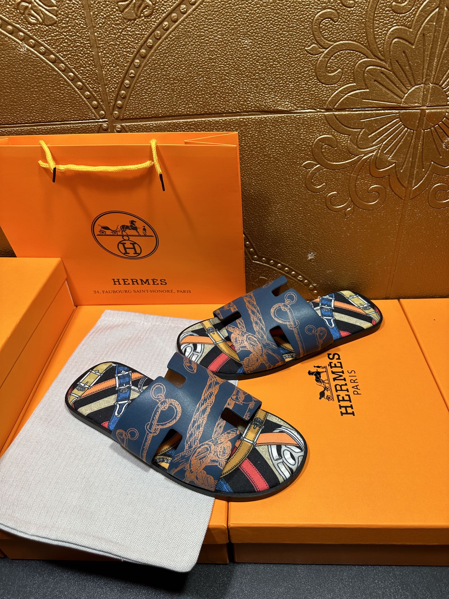 Blue Hermes logo slide sandals with patterned straps and open toe, diagonal view.