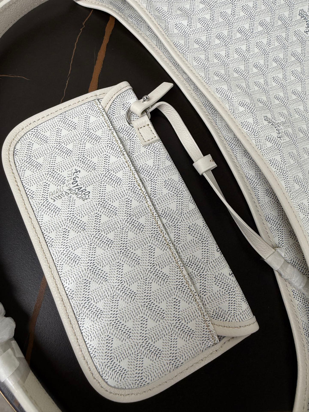 Goyard white zip pouch with monogram texture, leather trim, and front clasp.