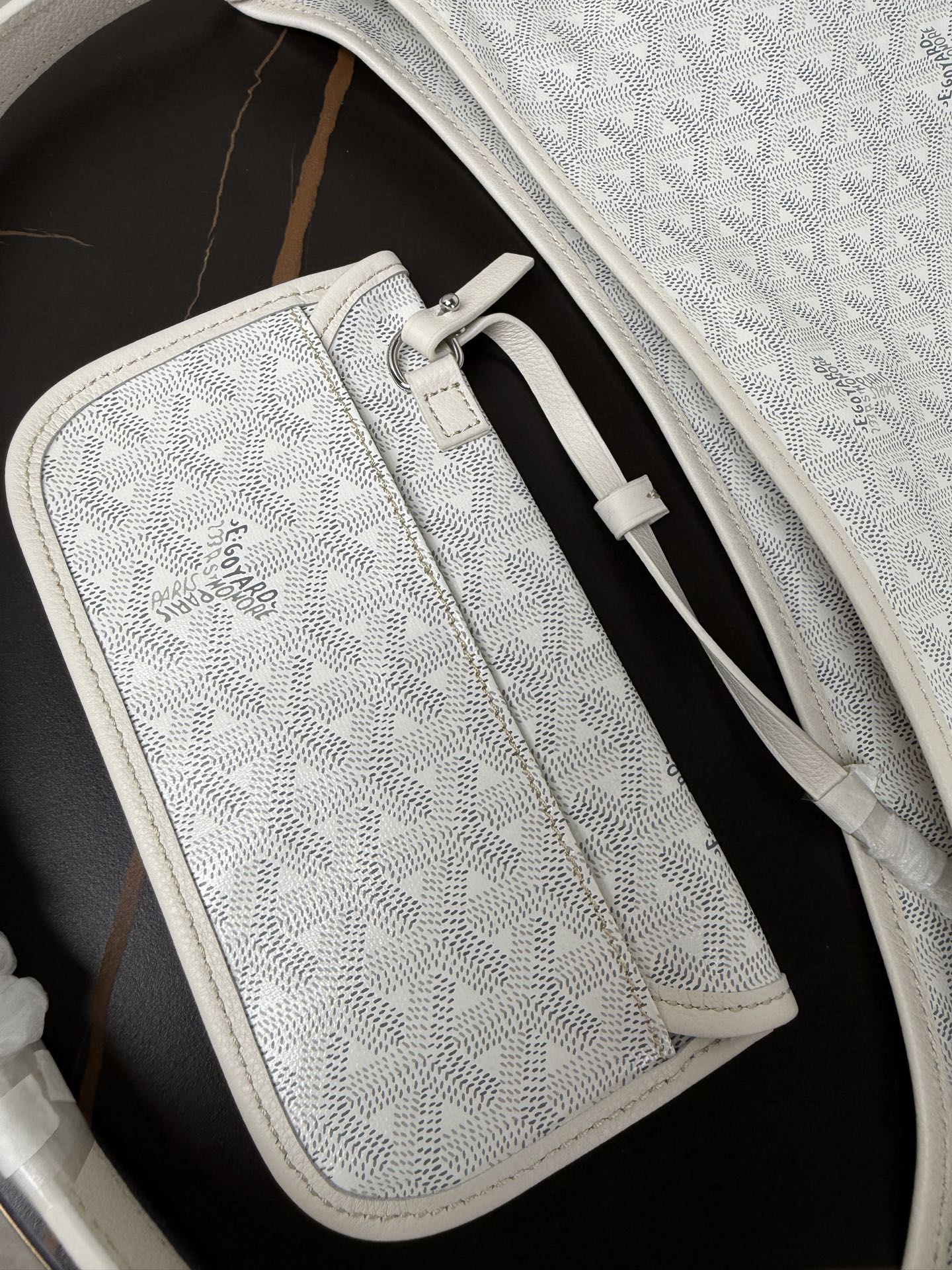 Goyard white zip pouch with monogram texture, leather trim, and front clasp.