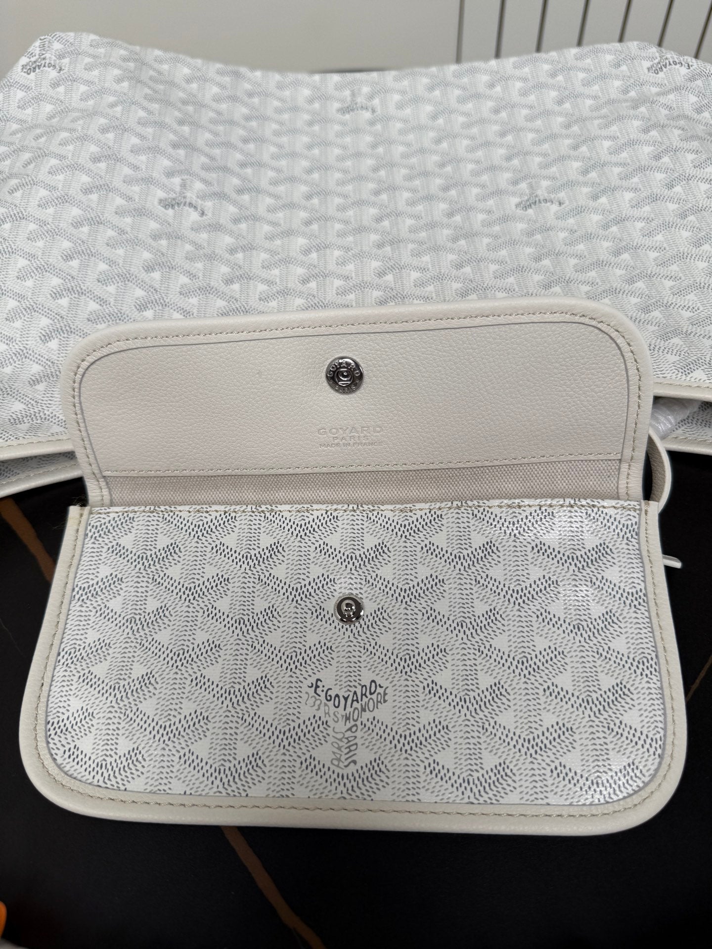 Goyard white mini pouch with monogram texture and leather flap with button.