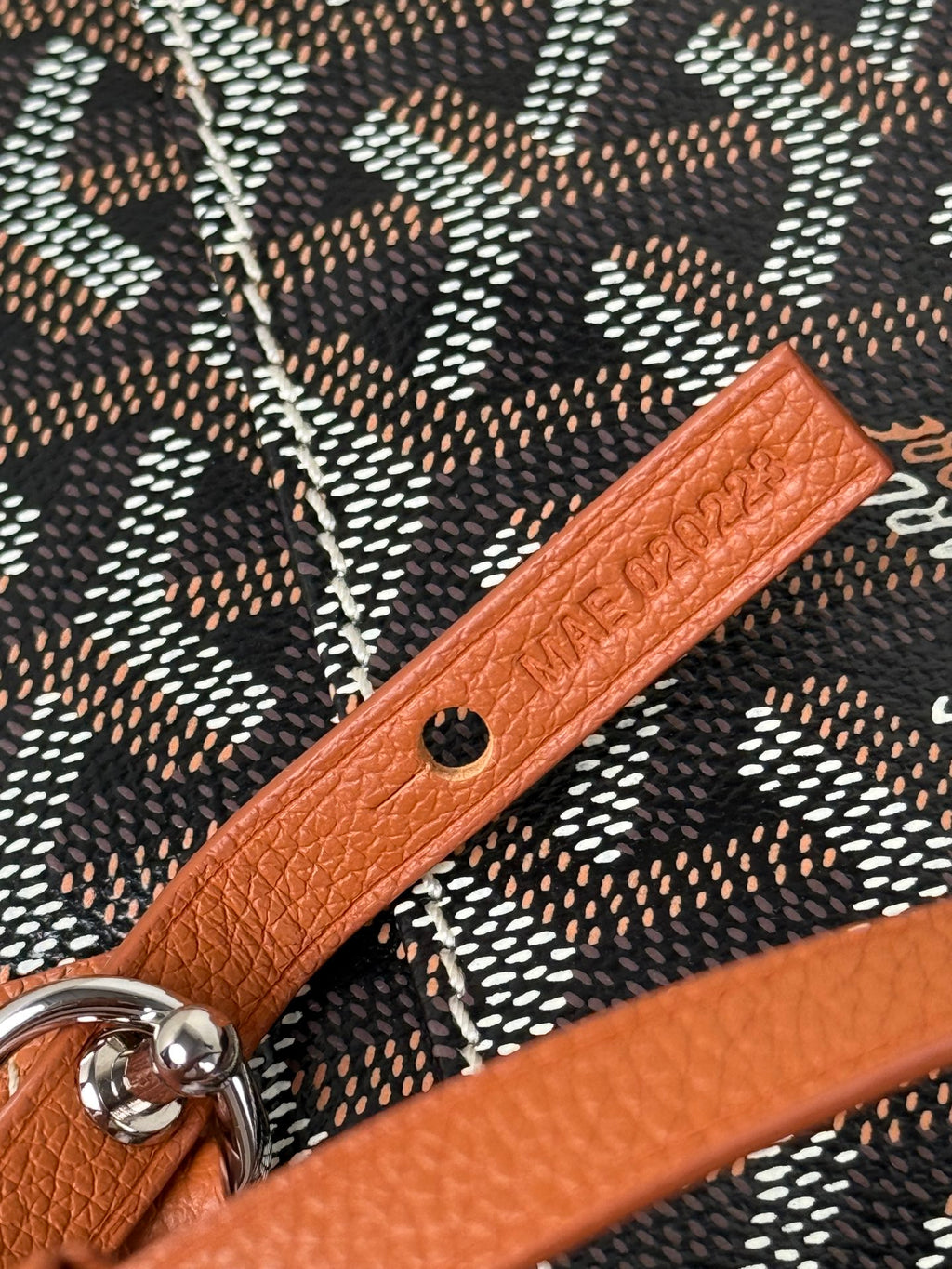 Goyard bag detail: tan leather strap with embossed text and metal snap hardware