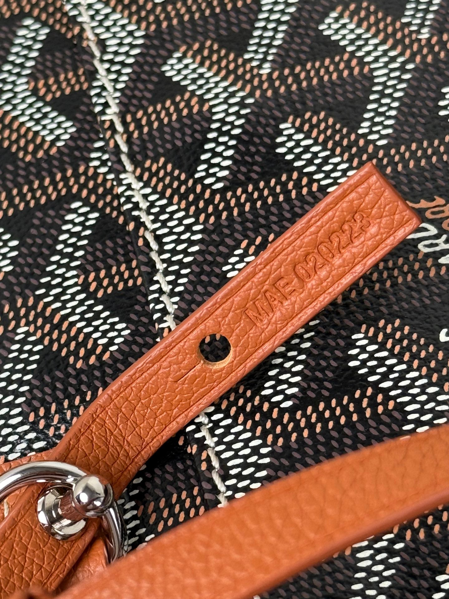 Goyard bag detail: tan leather strap with embossed text and metal snap hardware