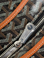 Goyard bag zipper close-up with clear pull tab, dark fabric, and orange leather trim