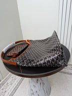Goyard hobo bag with dark monogram pattern, orange handle accents, and braided top