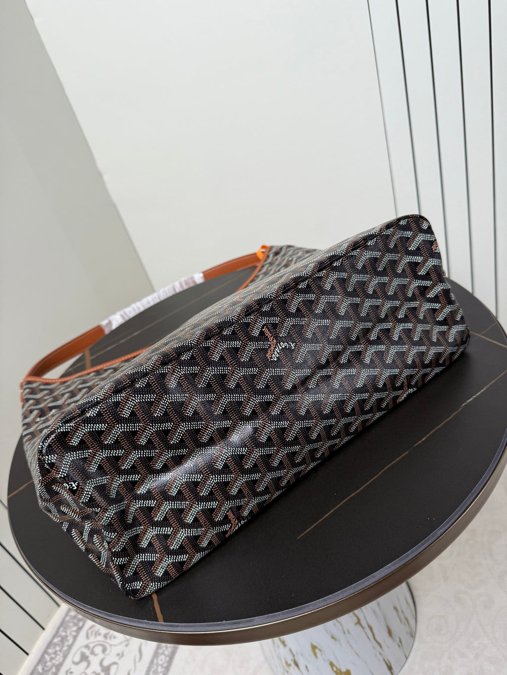 Goyard duffle-style bag with dark monogram pattern and orange-trimmed strap