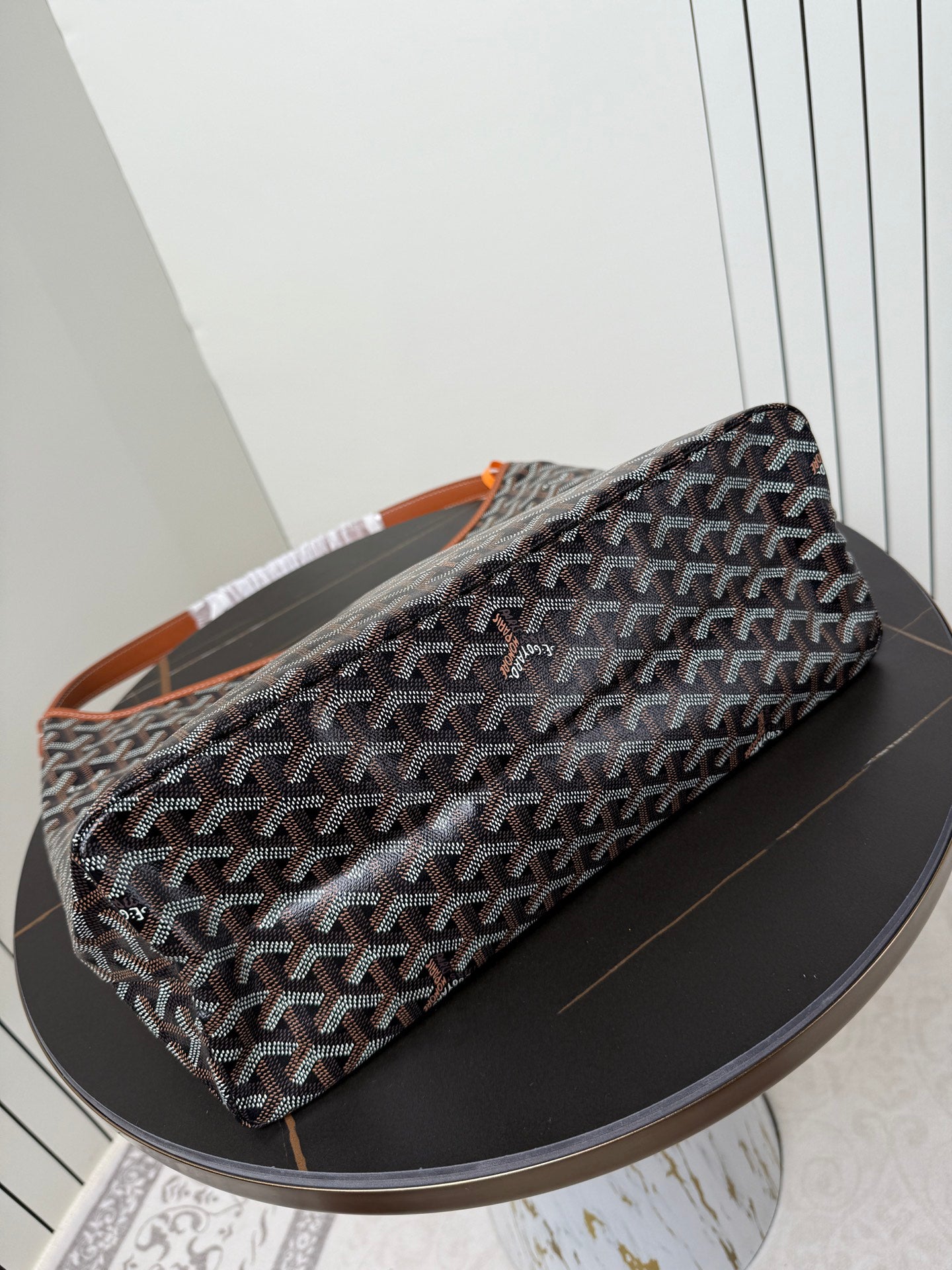 Goyard duffle-style bag with dark monogram pattern and orange-trimmed strap
