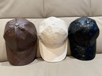 Three Louis Vuitton caps: brown, white, and dark blue/black on couch