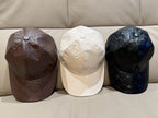 Three Louis Vuitton caps: brown, white, and dark monogram leather with curved brims
