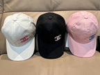 Three baseball caps: white, black, and pink with Chanel logo emblems.
