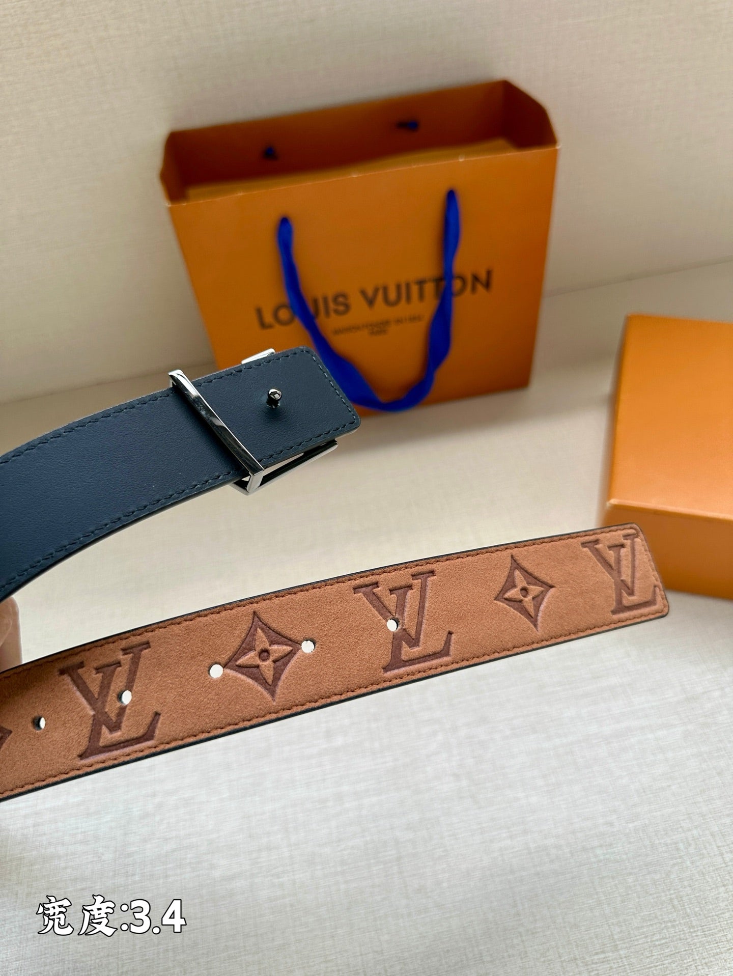 Monogram leather belt strap with gold-tone accents, set beside a blue leather belt piece