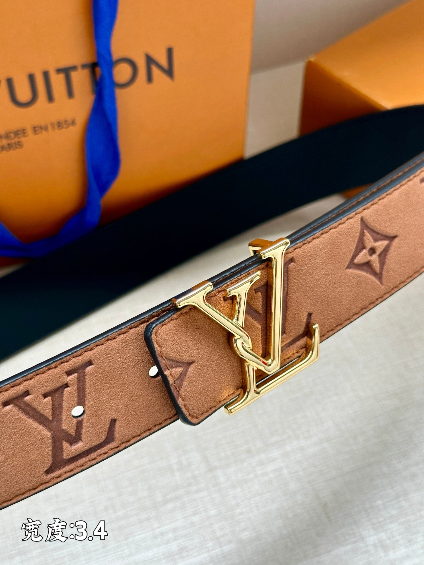 Close-up monogram belt with gold-tone V buckle and rectangular leather keeper on tan strap