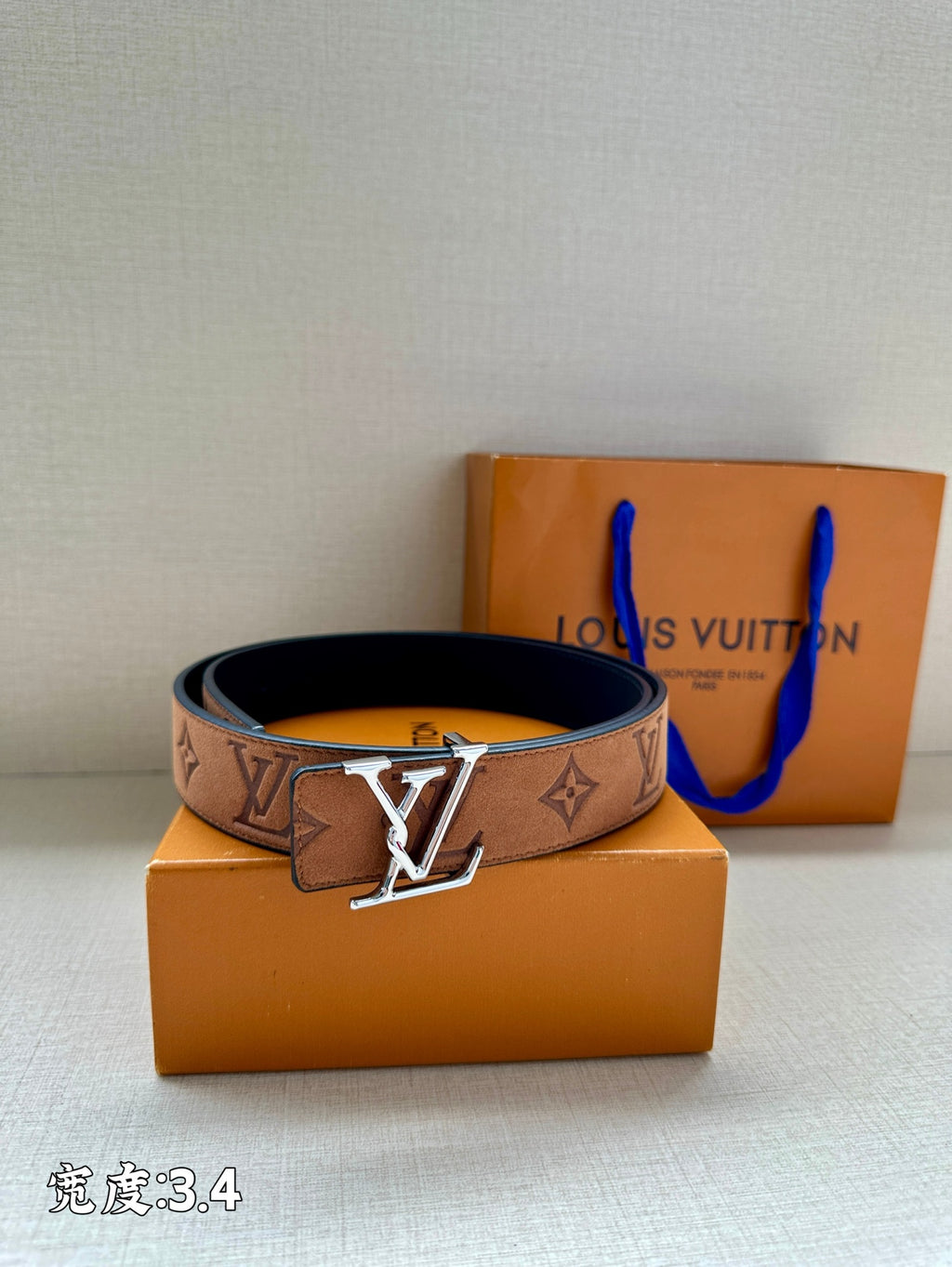 Tan/brown monogram belt with gold-tone V buckle and dark backing, laid on boxes