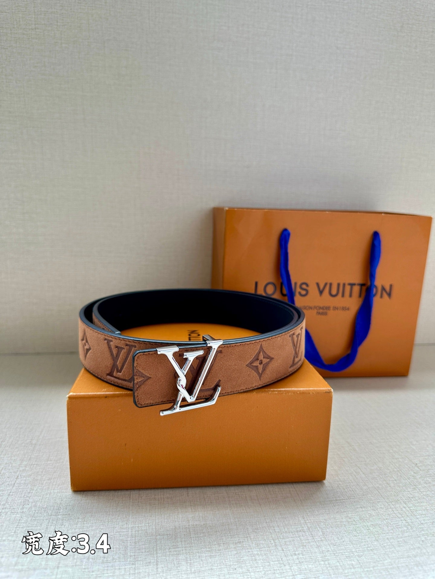 Tan/brown monogram belt with gold-tone V buckle and dark backing, laid on boxes