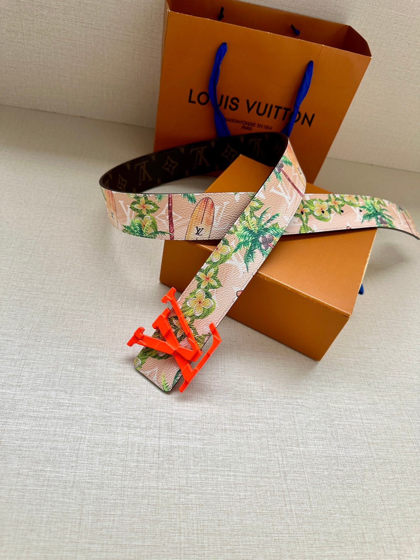 Louis Vuitton belt with floral fabric strap and large orange LV buckle, laid out