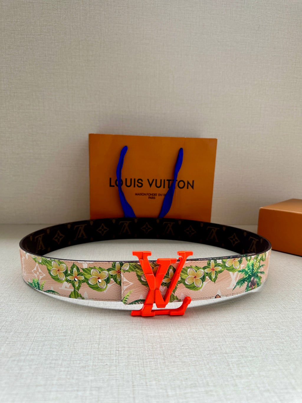 Louis Vuitton belt with floral strap and orange LV buckle on dark backing