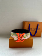 Louis Vuitton belt with floral strap and orange LV buckle on dark backing