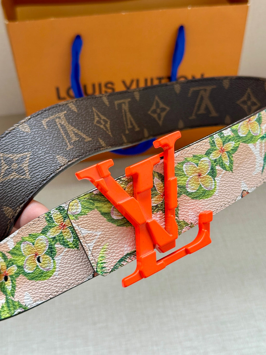 Louis Vuitton belt close-up: floral strap with orange LV buckle over dark monogram