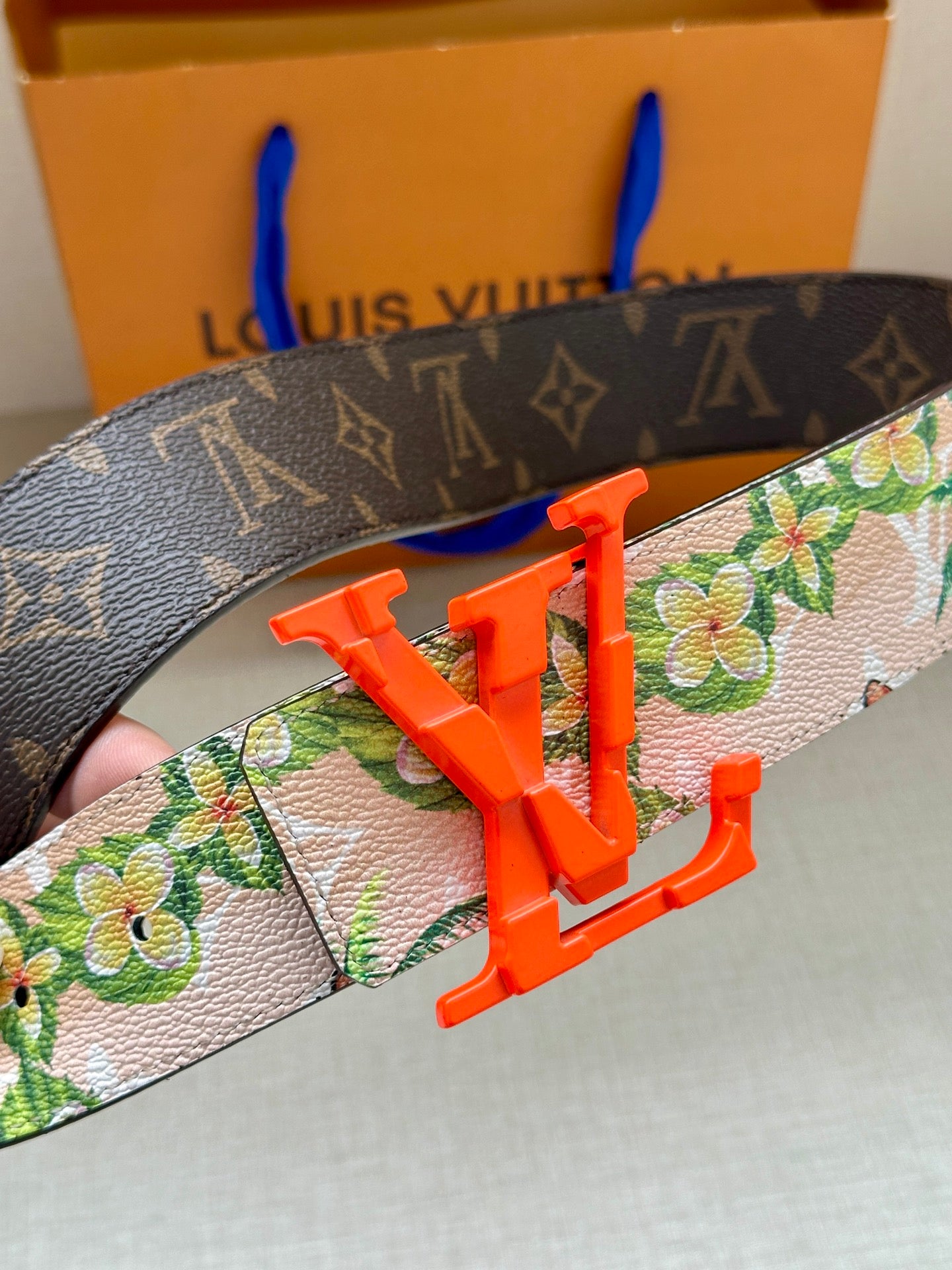Louis Vuitton belt close-up: floral strap with orange LV buckle over dark monogram
