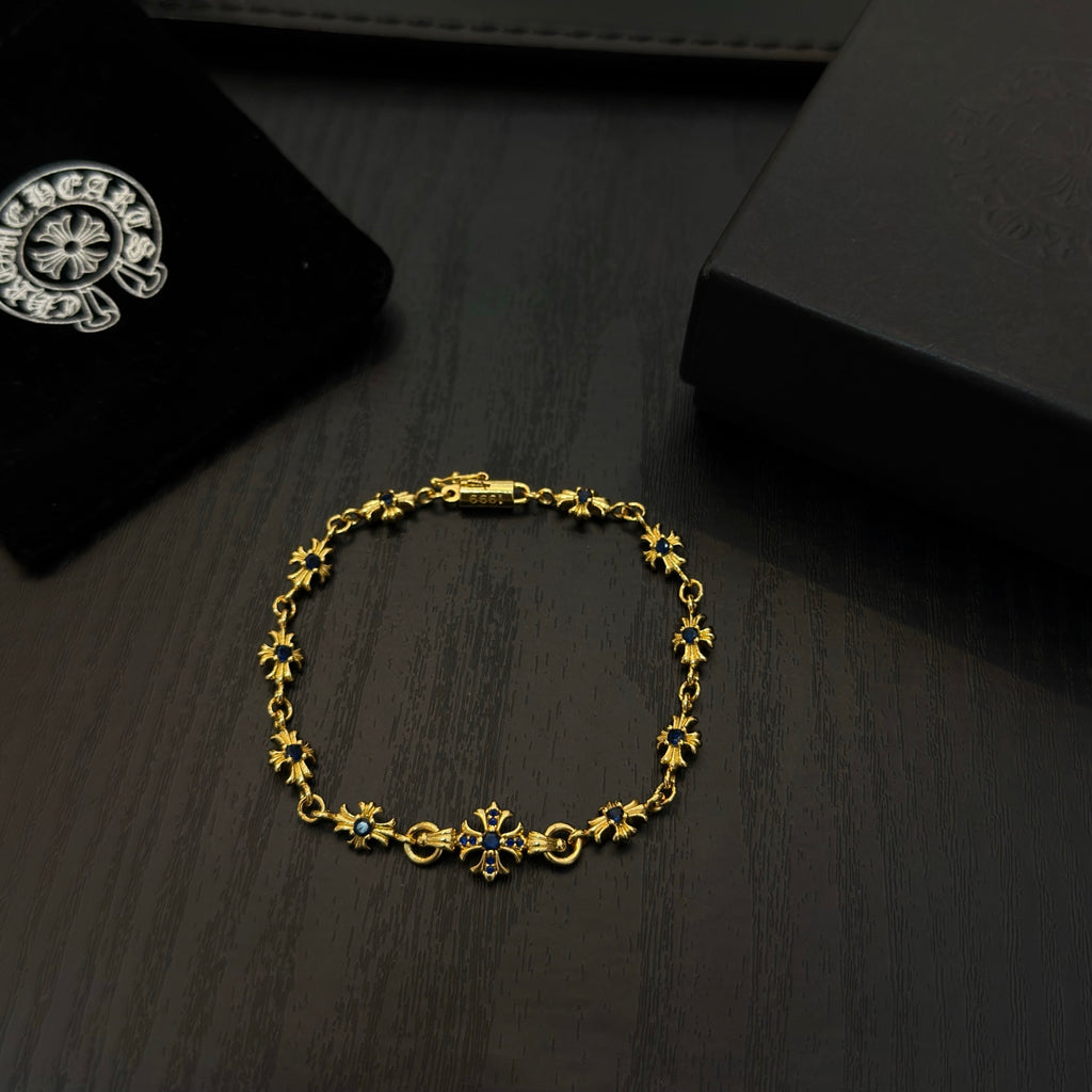 Gold charm bracelet with blue flower beads on a dark wood surface.