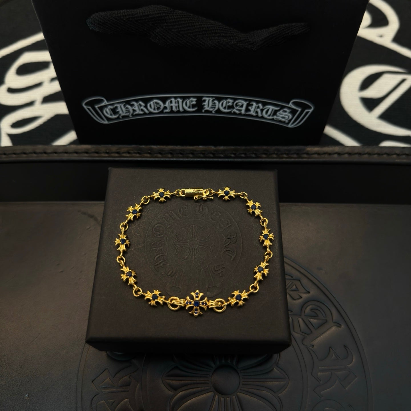 Gold charm bracelet with blue flower beads, laid on a black gift box.