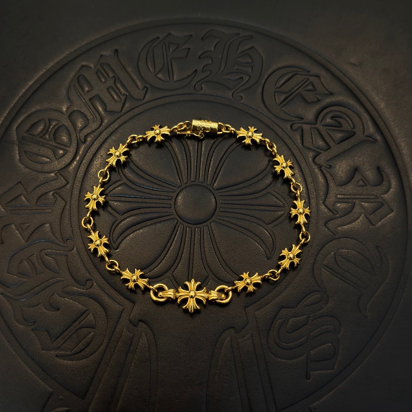 Gold charm bracelet with blue flower beads, centered on a dark embossed coaster.