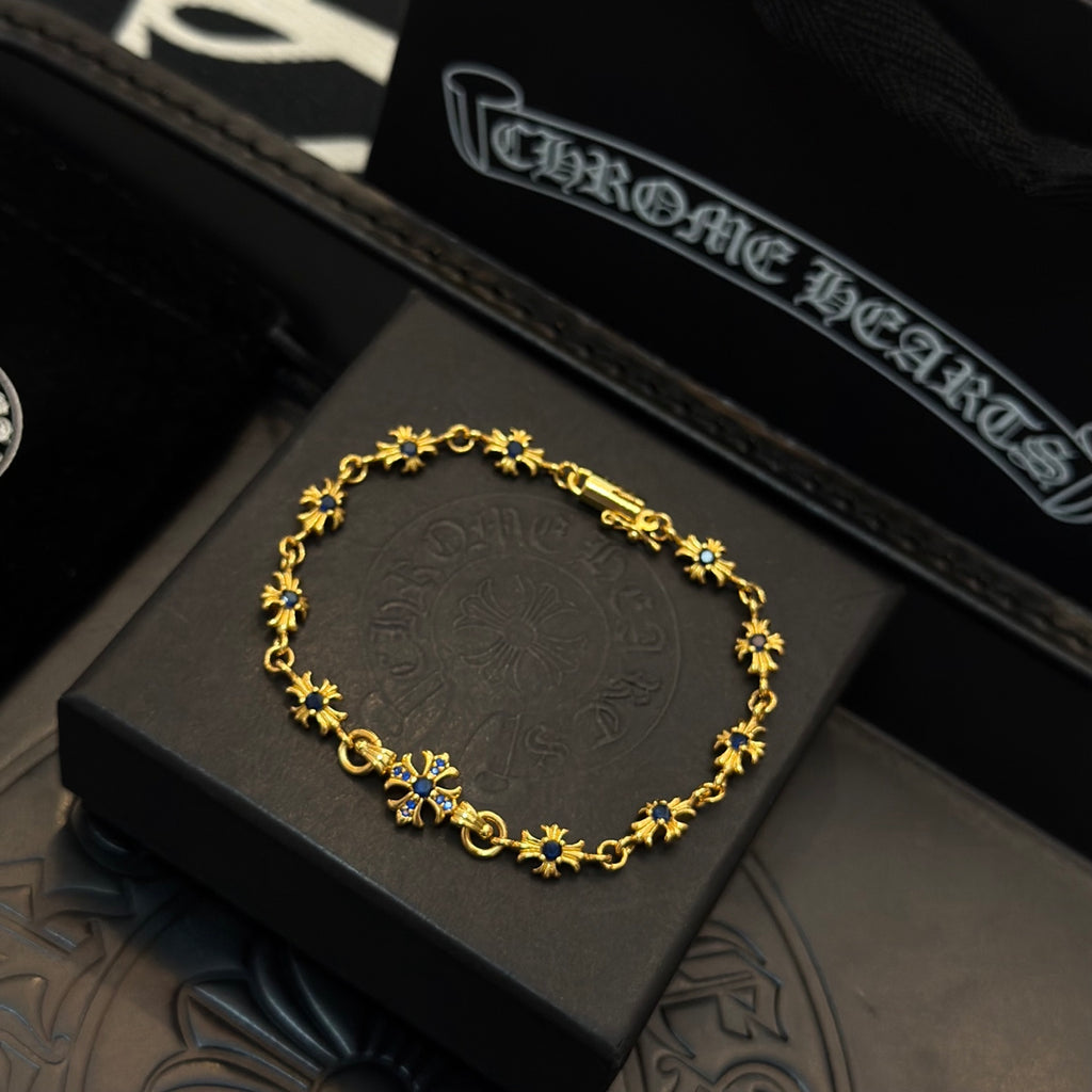 Gold charm bracelet with blue flower accents, shown in a dark display box.