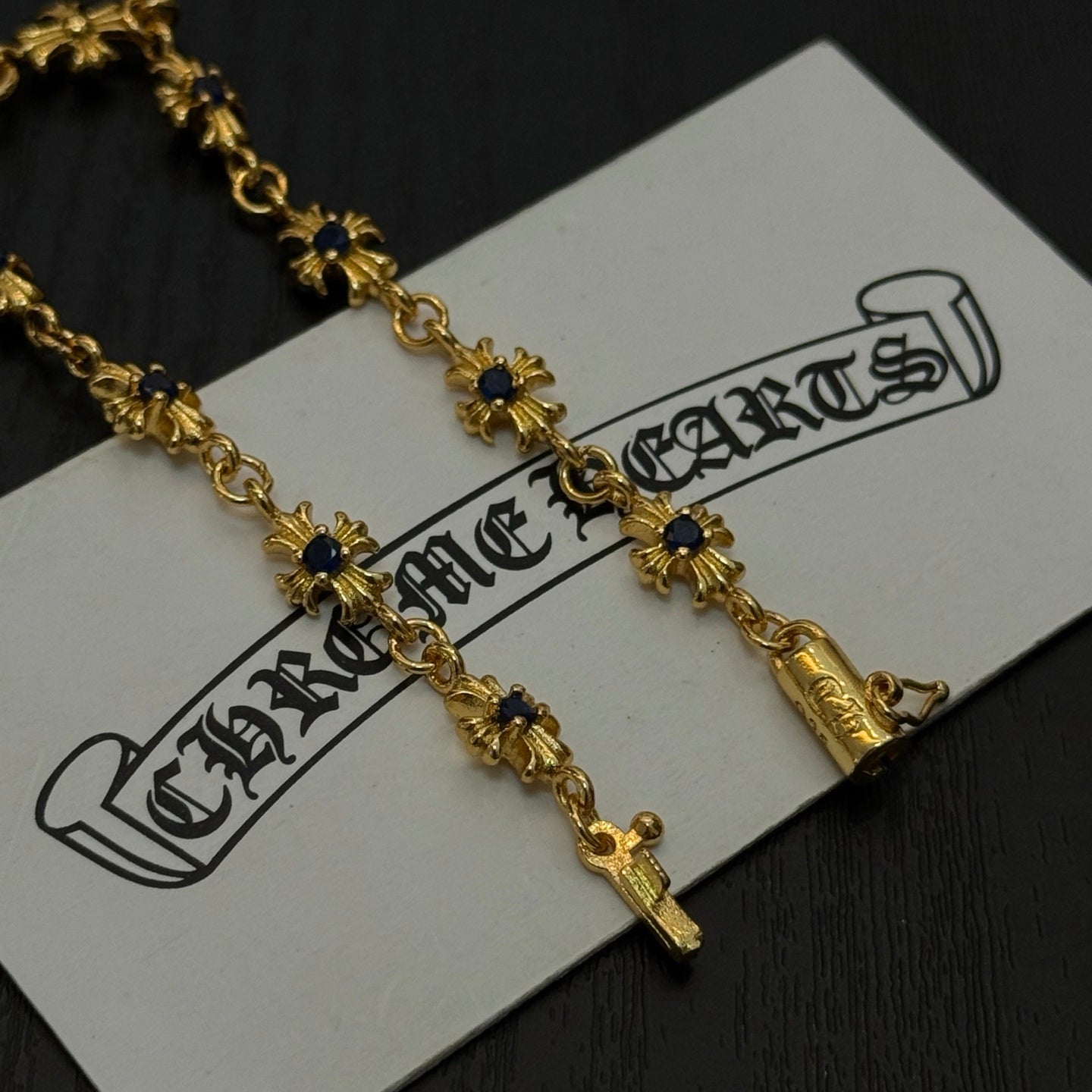 Gold charm bracelet with blue flower charms on a white product tag, close up.