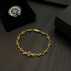 Gold charm bracelet with blue flower beads, resting on dark wood near a box.