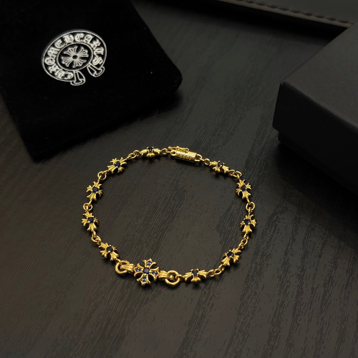 Gold charm bracelet with blue flower beads, resting on dark wood near a box.