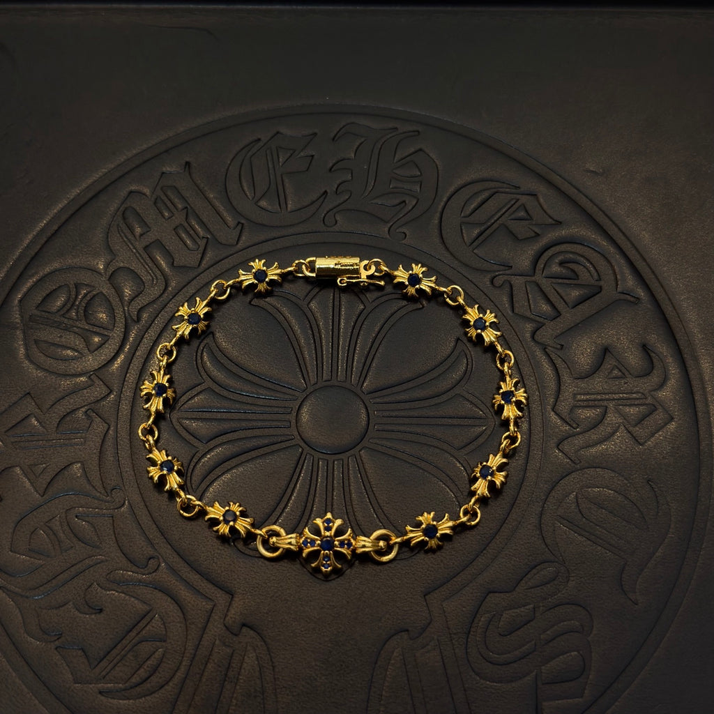 Gold charm bracelet with blue flower beads on a dark embossed coaster.