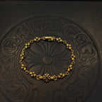 Gold charm bracelet with blue flower beads on a dark embossed coaster.