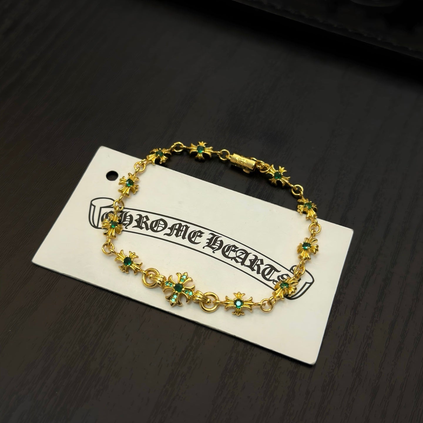 Gold-tone link bracelet with green flower charms on a white backing card