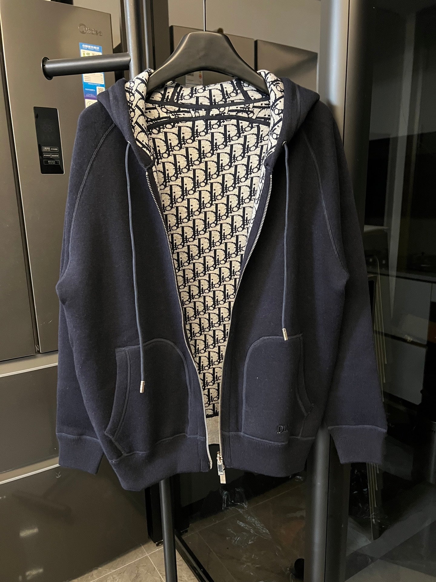 Navy zip-up hoodie with hood and Dior monogram lining, front view.