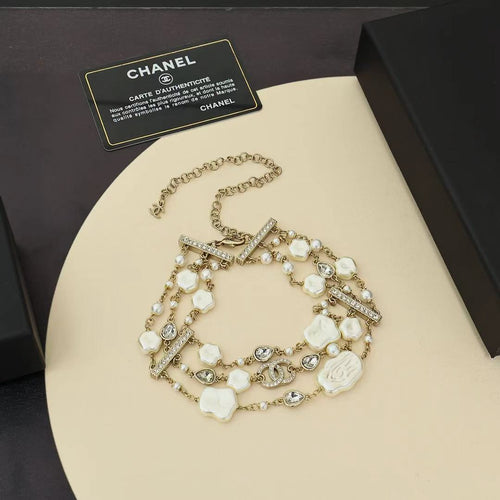 Charm bracelet with gold-tone links, white shell beads, pearls, and crystal accents
