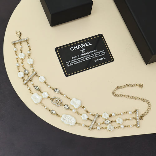 Multi-strand charm bracelet with pearl beads, white shell charms, and crystal bar details