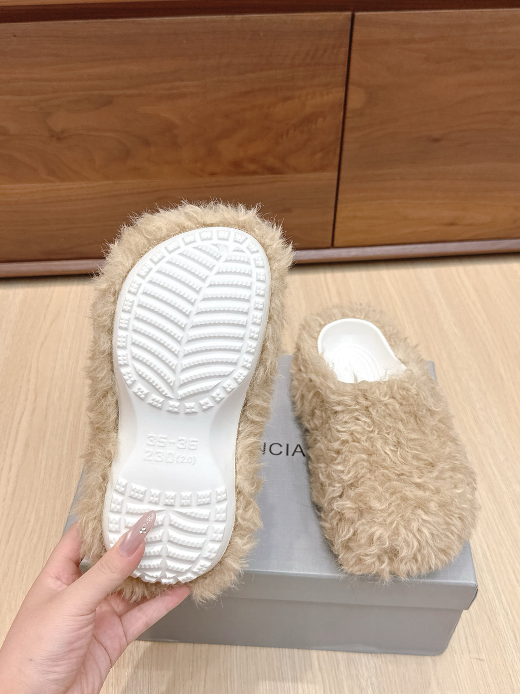 Beige faux-fur slide sandal with textured white outsole, hand holding sole