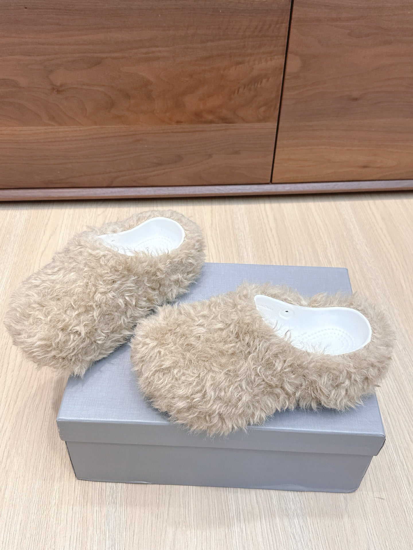 Beige faux-fur slide sandals on gray box, angled view