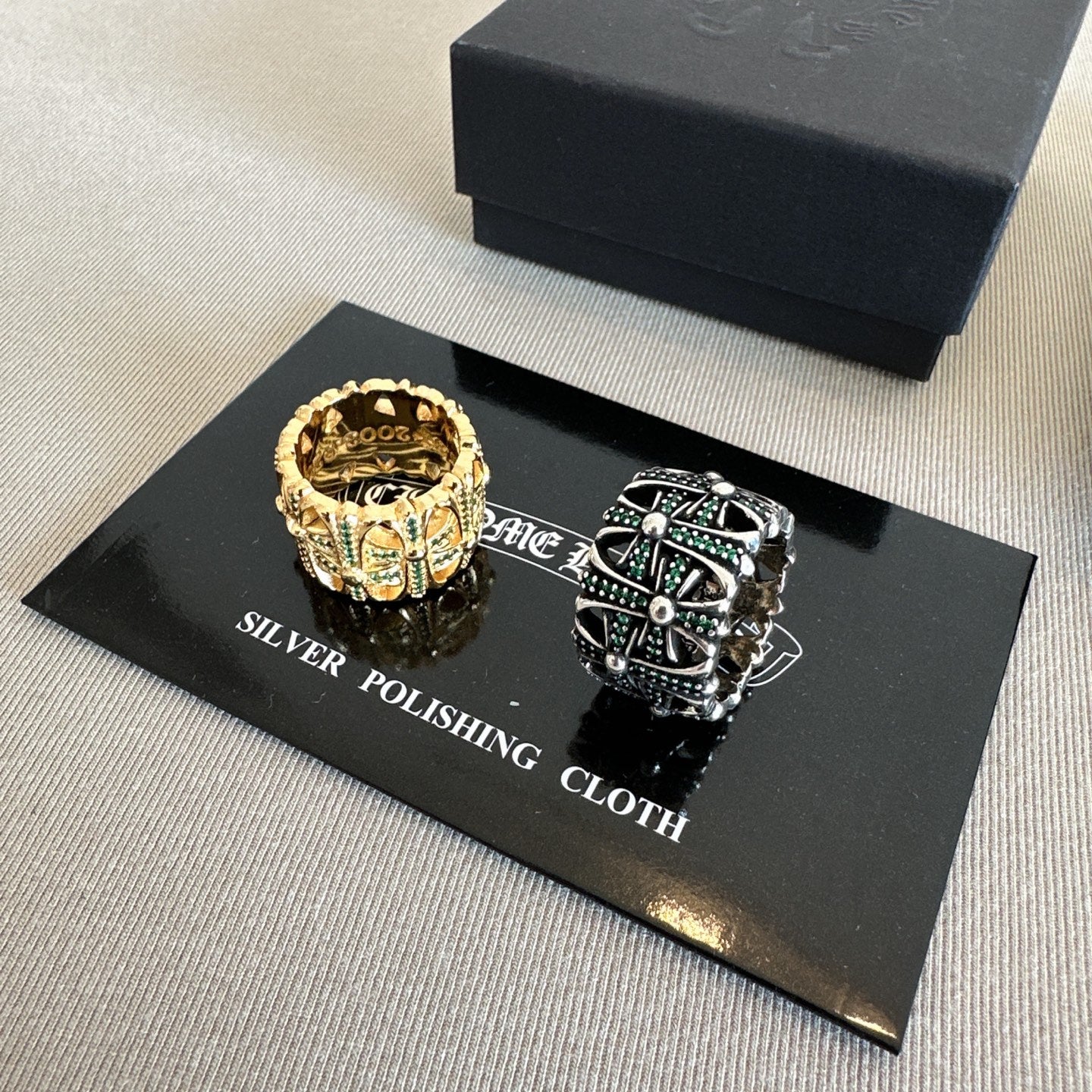 Chrome accessories rings on polishing cloth card, gold crown-style ring and silver tone ring