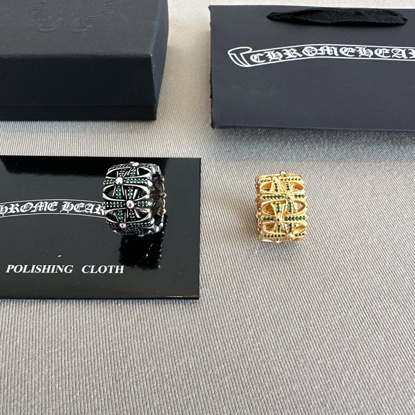 Chrome accessories rings beside polishing cloth card, black ring with green stones and gold ring