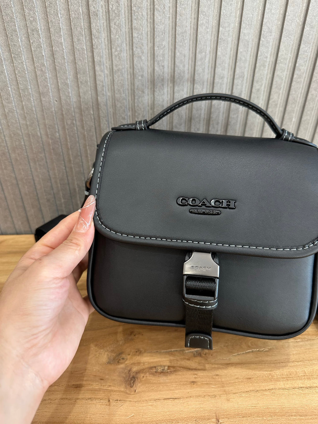 Black flap crossbody bag close-up with logo, stitched trim, and buckle clasp
