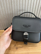 Black flap crossbody bag close-up with logo, stitched trim, and buckle clasp