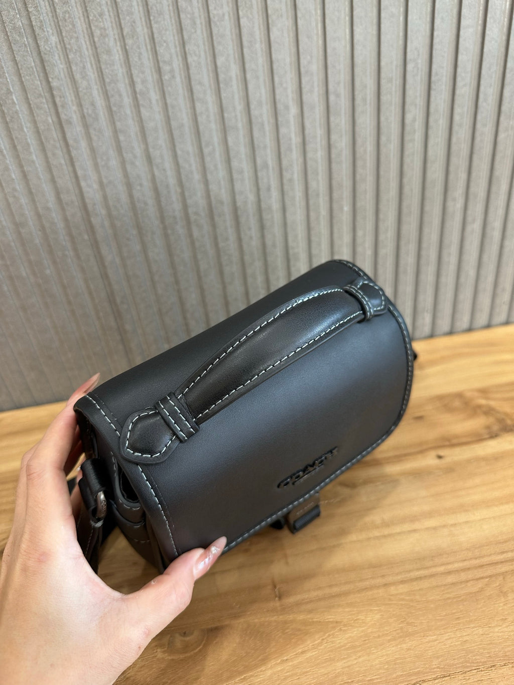 Black crossbody bag side with stitched strap loop and metal hardware