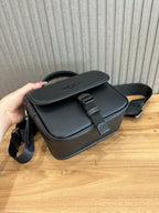 Black crossbody bag with flap, front buckle strap, and visible side seams