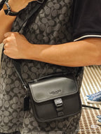 Black small crossbody bag worn on patterned dress, front flap with buckle