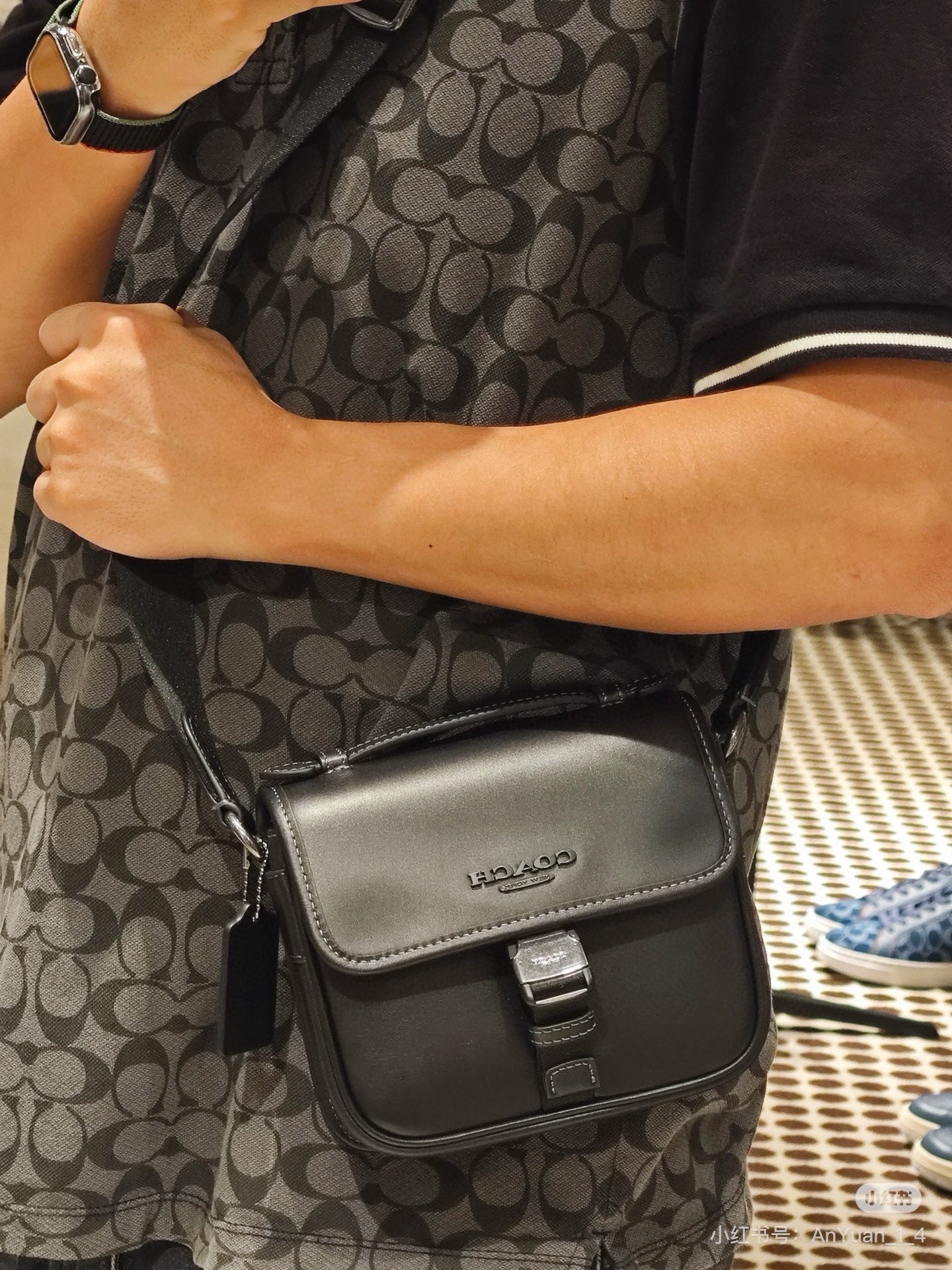 Black small crossbody bag worn on patterned dress, front flap with buckle