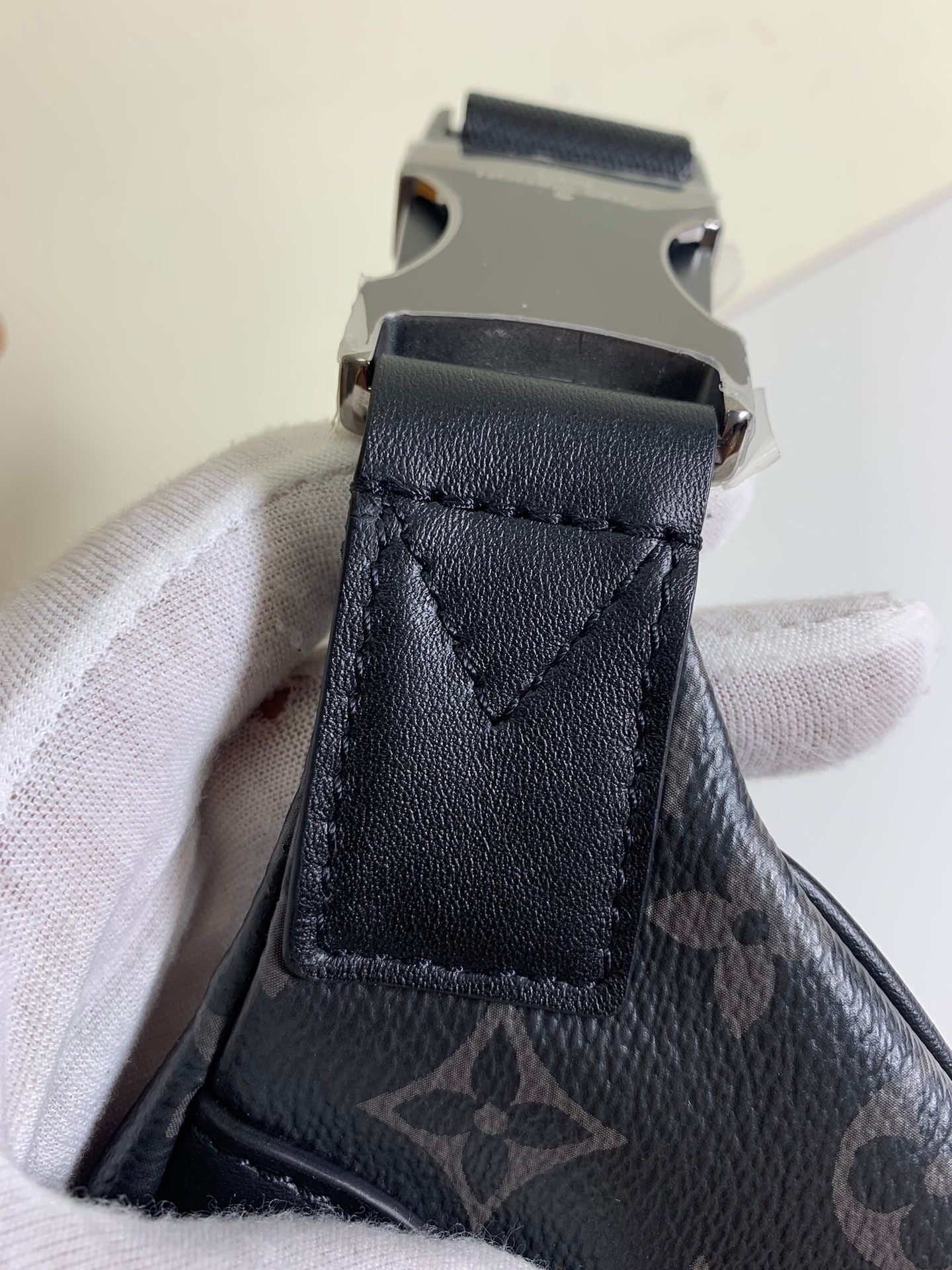 Black monogram belt bag strap end with metal buckle and stitched leather tab