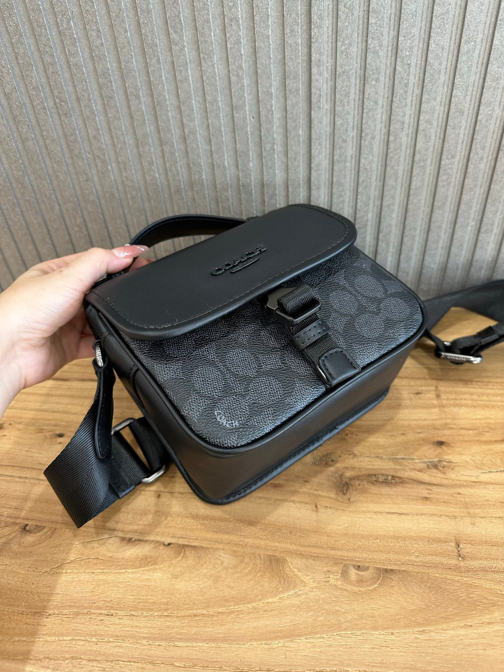Coah crossbody bag angled; black leather flap and trim, dark patterned base, side strap