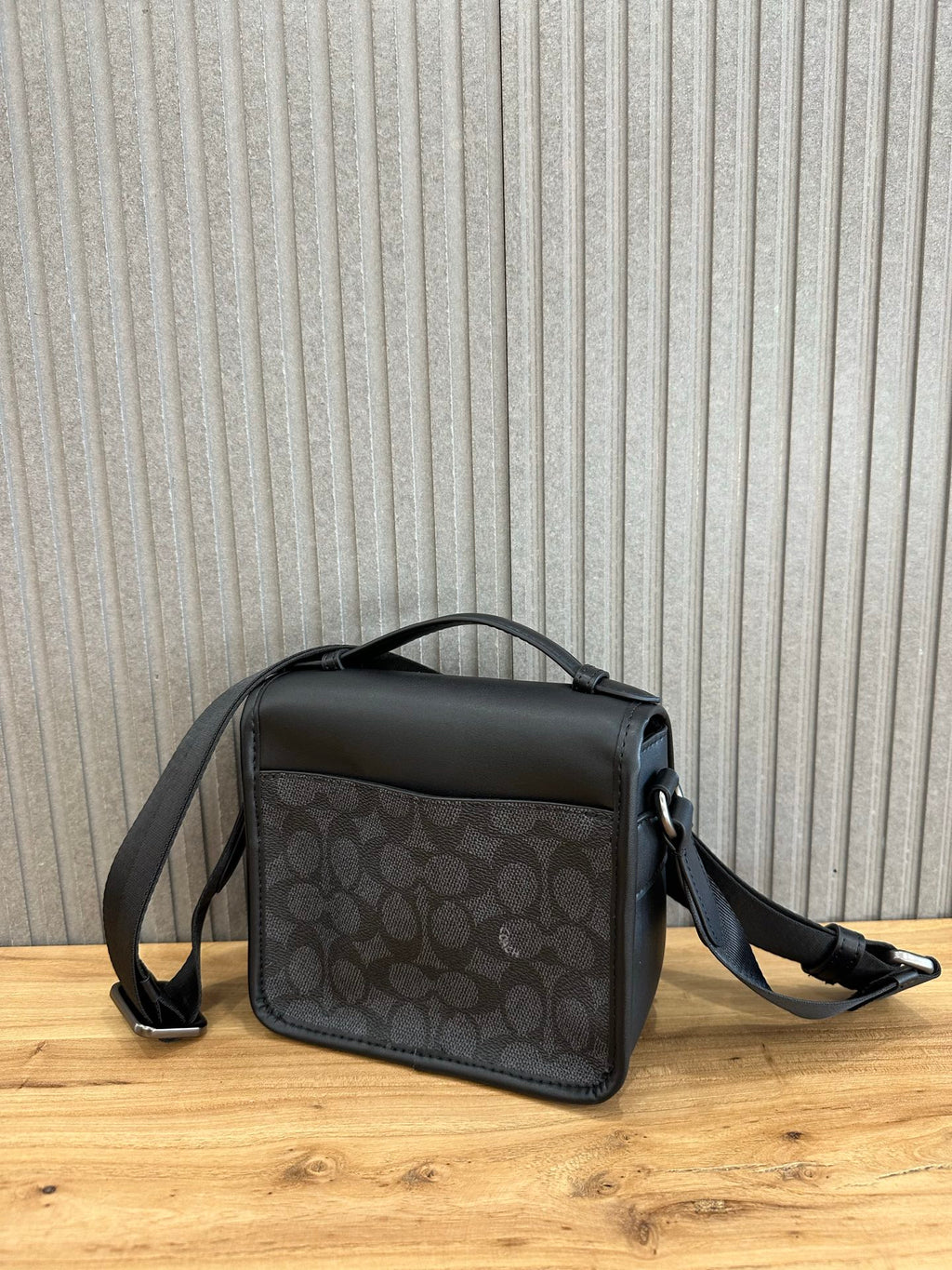 Coah crossbody bag front view; black top flap, dark patterned body, shoulder strap